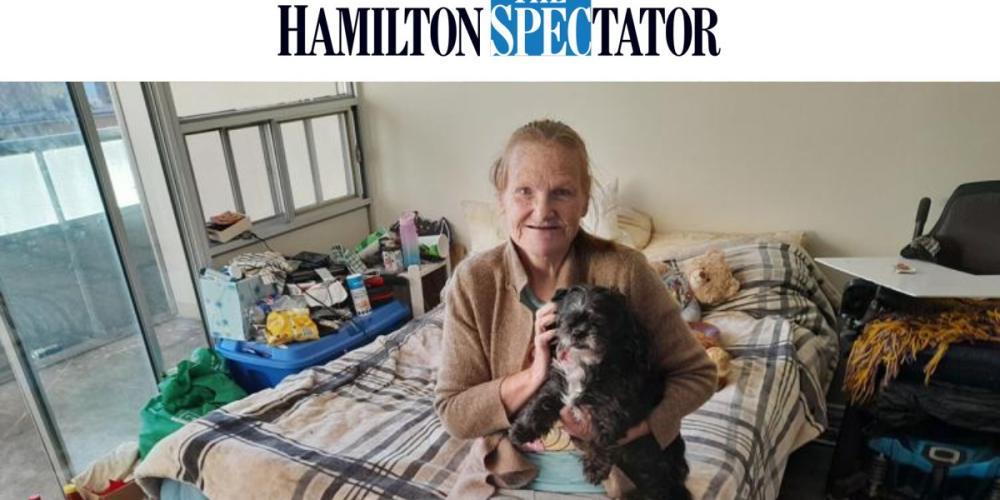 An older woman sits on a bed holding a small black dog. The Hamilton Spectator logo appears at the top of the image.