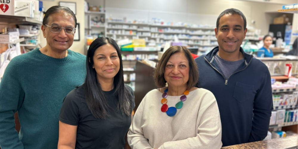 The Sandhu family smiling together with their pharmacy in the background.