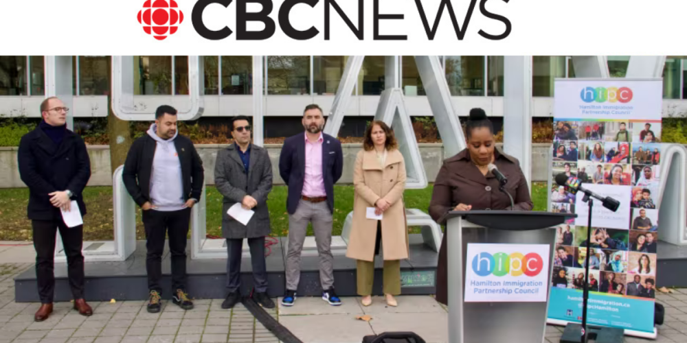 A group of people, including Wesley CEO Rashed Afif, stand outside near a podium labeled Hamilton Immigration Partnership Council during a CBC News event. A woman is speaking at the podium.