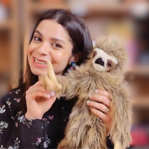Dema, wearing a floral top smiles while holding a stuffed sloth.